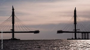 Construction of the Cable-Stayed Bridge. Construction of a large cable-stayed bridge against the backdrop of the sea bay at sunset